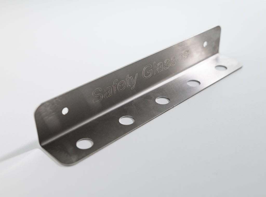 Metal corner bracket with 'Safety Glasses' engraving. The TLC Glasses Holder 5 Slot keeps safety glasses organized, visible, and accessible in Lean workplaces. Ideal for factories, warehouses, workshops, and production areas, it minimizes loss, damage, and clutter. With five slots, it supports shared use and proper PPE storage, reinforcing safety habits and aligning with 5S and 6S standards. A simple solution for improving PPE organization and workplace safety.
