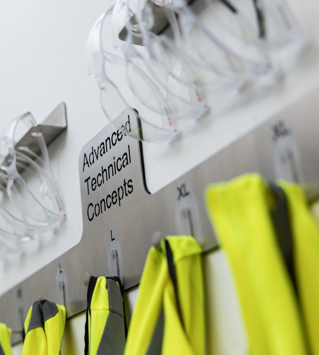 Yellow safety vests and gloves hanging on a rack. The TLC Hi Viz Holder 5 Hangers keeps high visibility vests organized, accessible, and easily identifiable in Lean workplaces. It provides a dedicated storage solution for shared PPE in factories, warehouses, workshops, and site offices. This holder helps reduce clutter, prevent loss, and supports 5S and 6S safety standards. Ideal for entrances, locker areas, and workstations.